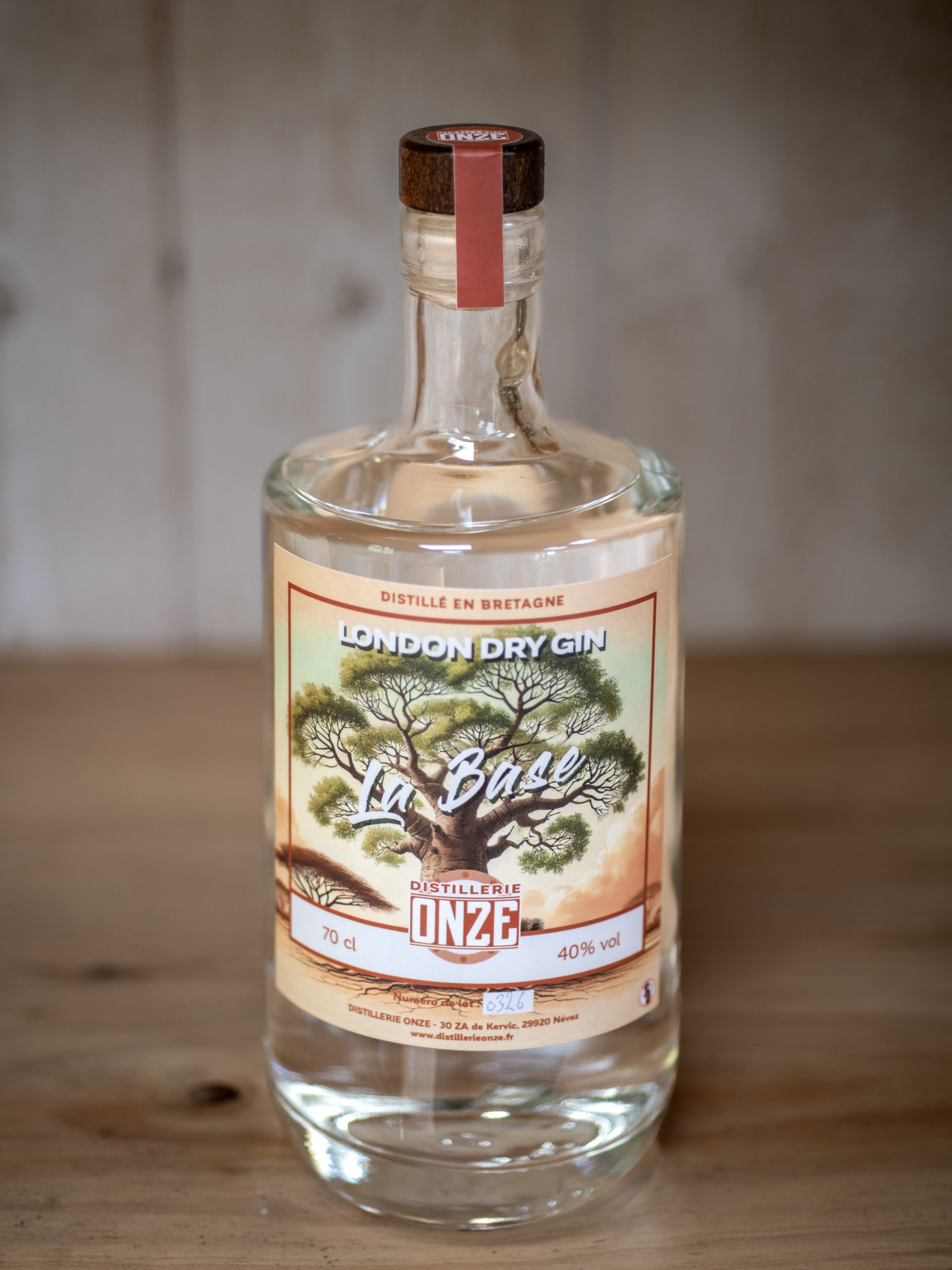 Bouteille de gin London Dry Gin "La Base" de la distillerie Onze, posée sur une table en bois.