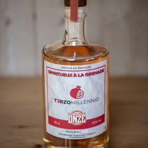 Bouteille de spiritueux "Terzo Millennio" à la grenade de la distillerie Onze, posée sur une table en bois.